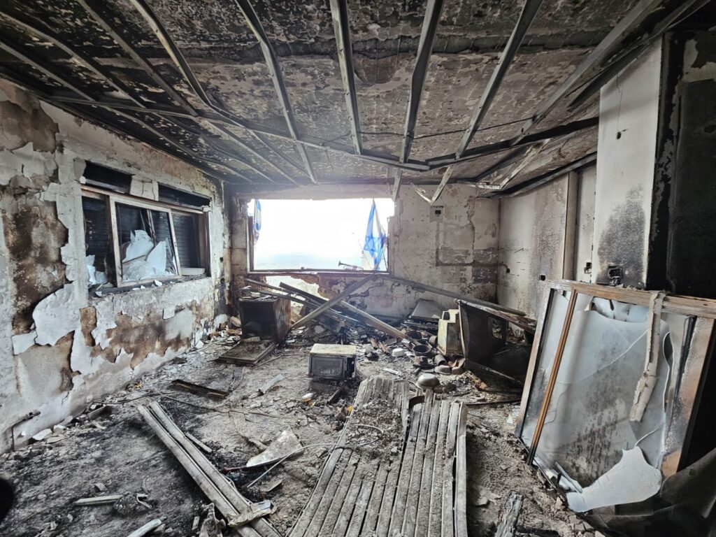 A burnt-out room with a collapsed ceiling and debris, flags hanging in the window opening